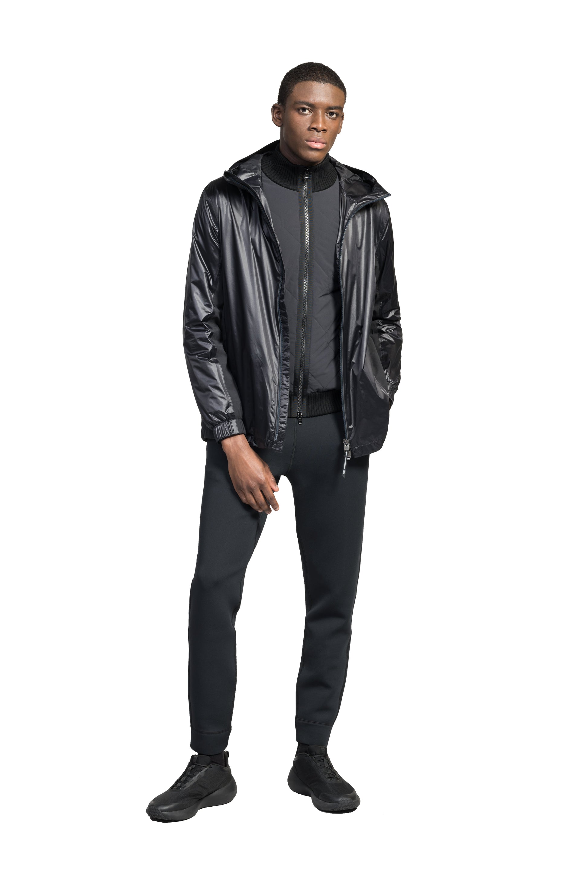 Stratus Men's Tailored Packable Rain Jacket in hip length, premium cire technical nylon taffeta and stretch ripstop fabrication, highly breathable mesh lining, hidden packable pocket, non-removable hood with adjustable draw cord, reflective piping along front and back, underarm grommets for extra breathability, back yoke with mesh ventilation, two waist zipper pockets, two interior zipper pockets, elastic cuffs with adjustable snap button, and adjustable interior draw cord at waist hem, in Black