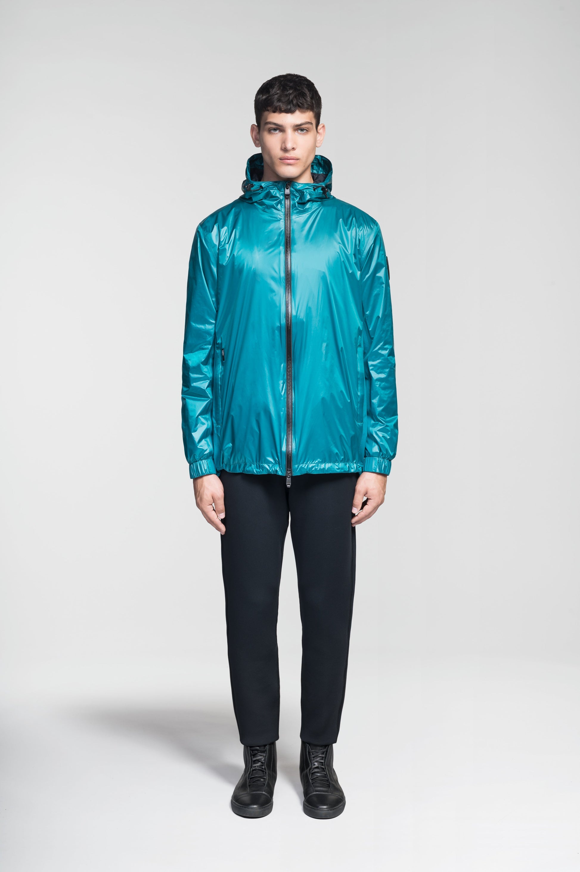 Stratus Men's Tailored Packable Rain Jacket in hip length, premium cire technical nylon taffeta and stretch ripstop fabrication, highly breathable mesh lining, hidden packable pocket, non-removable hood with adjustable draw cord, reflective piping along front and back, underarm grommets for extra breathability, back yoke with mesh ventilation, two waist zipper pockets, two interior zipper pockets, elastic cuffs with adjustable snap button, and adjustable interior draw cord at waist hem, in Deep Lake