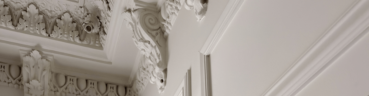 White decorative interior wall molding and ornate ceiling cornices in a classic architectural style.