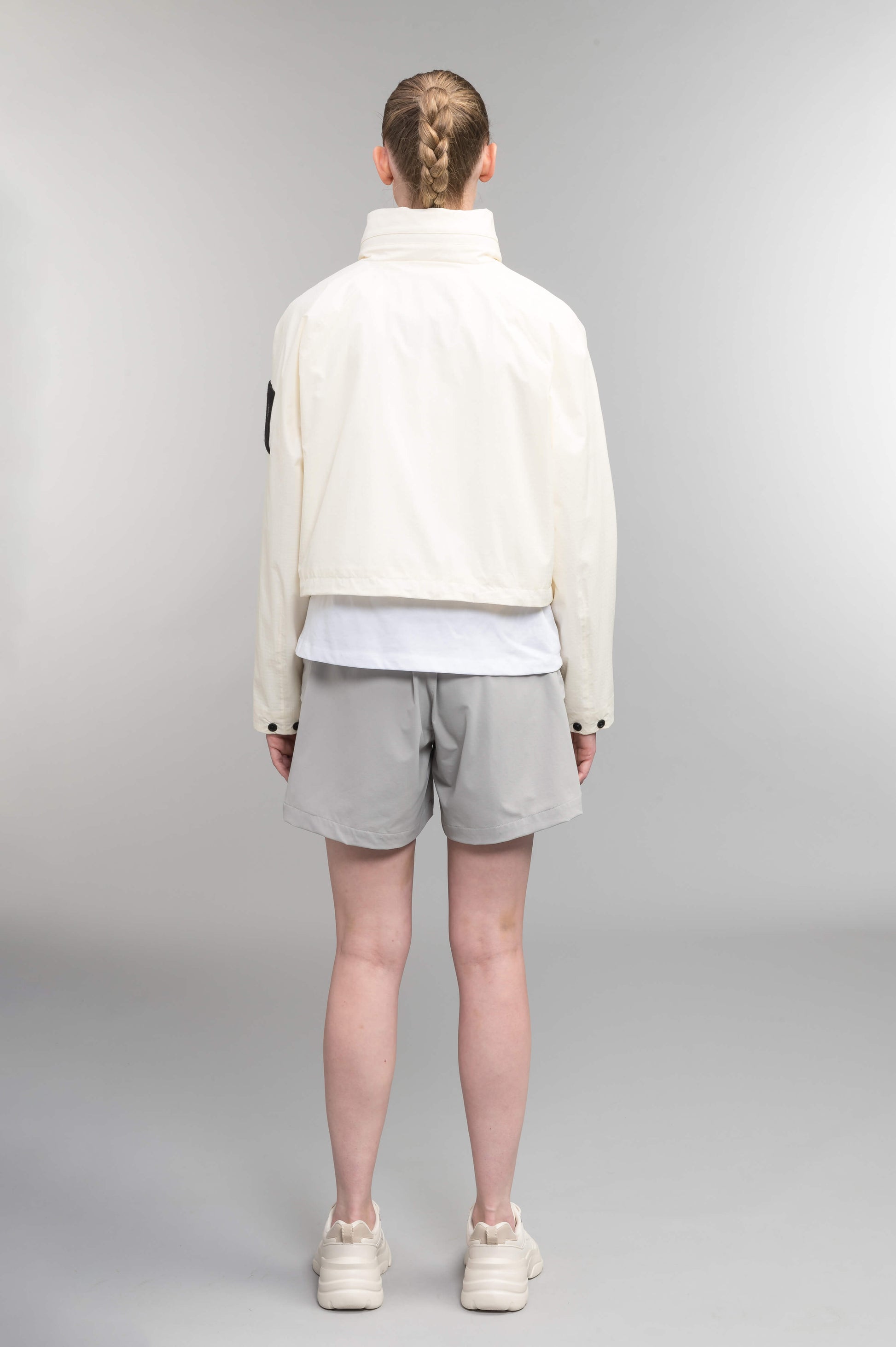 Epsie Women's Cropped Rain Jacket in Chalk crafted from premium recycled polyester ripstop with a DWR coating and taffeta nylon lining. Features a hidden packaway hood stored in the collar, two-way waterproof front zipper, seam-sealed construction, underarm zip ventilation, adjustable drawcord hem, zippered waist patch pockets, and an interior chest pocket for secure storage. Machine washable. Designed in Canada.