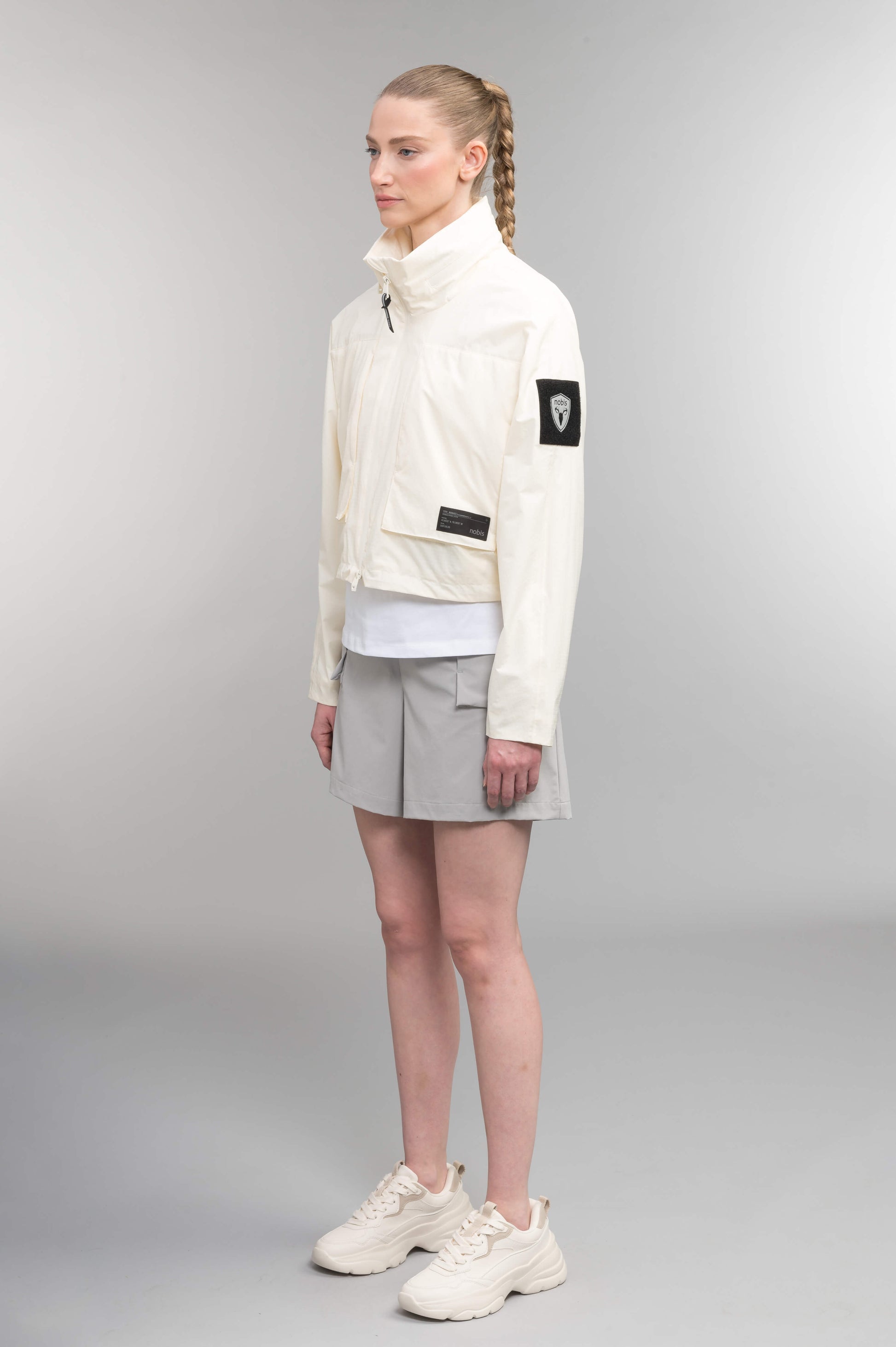 Epsie Women's Cropped Rain Jacket in Chalk crafted from premium recycled polyester ripstop with a DWR coating and taffeta nylon lining. Features a hidden packaway hood stored in the collar, two-way waterproof front zipper, seam-sealed construction, underarm zip ventilation, adjustable drawcord hem, zippered waist patch pockets, and an interior chest pocket for secure storage. Machine washable. Designed in Canada.