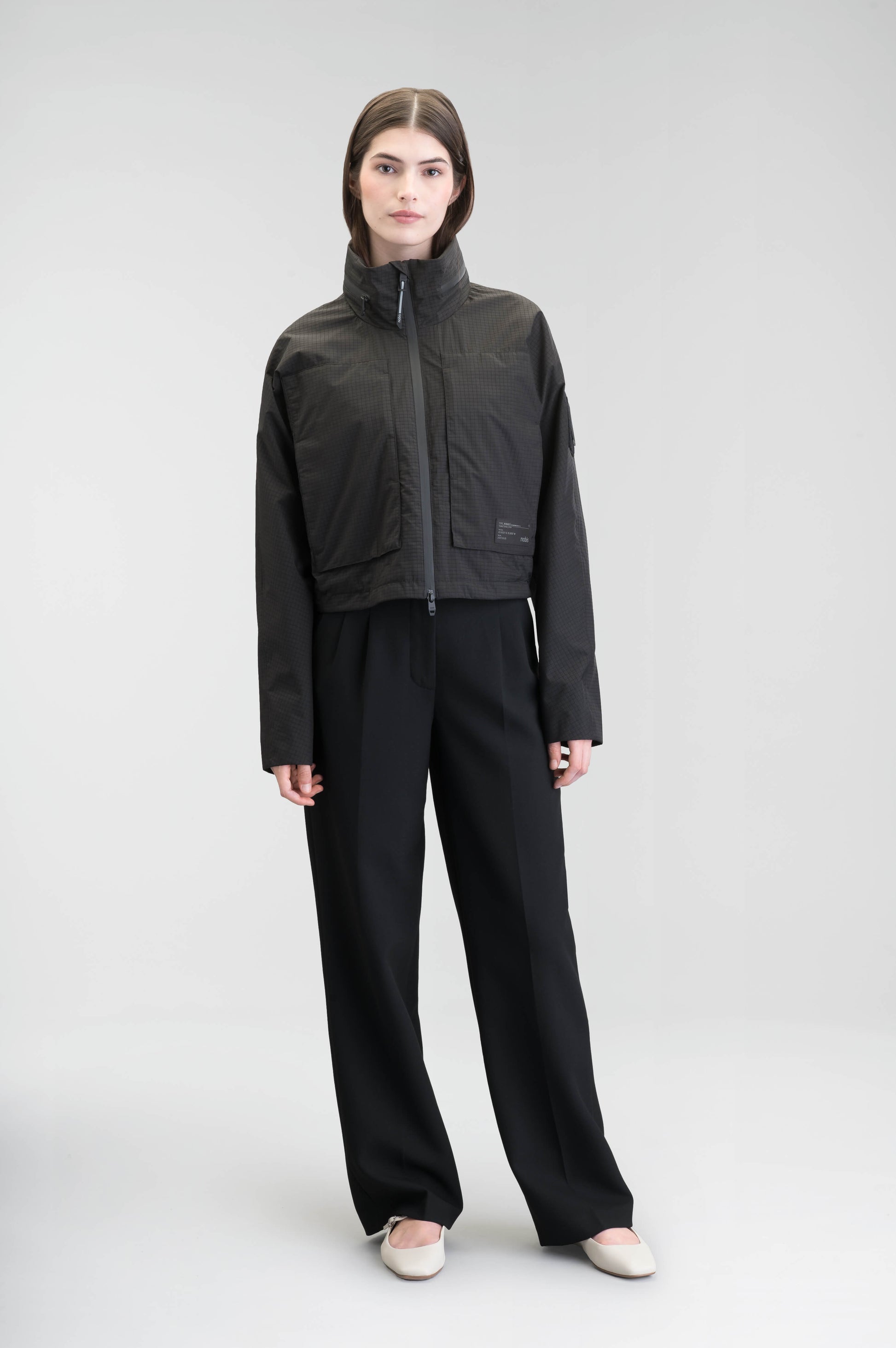 Epsie Women's Cropped Rain Jacket in Black crafted from premium recycled polyester ripstop with a DWR coating and taffeta nylon lining. Features a hidden packaway hood stored in the collar, two-way waterproof front zipper, seam-sealed construction, underarm zip ventilation, adjustable drawcord hem, zippered waist patch pockets, and an interior chest pocket for secure storage. Machine washable. Designed in Canada.