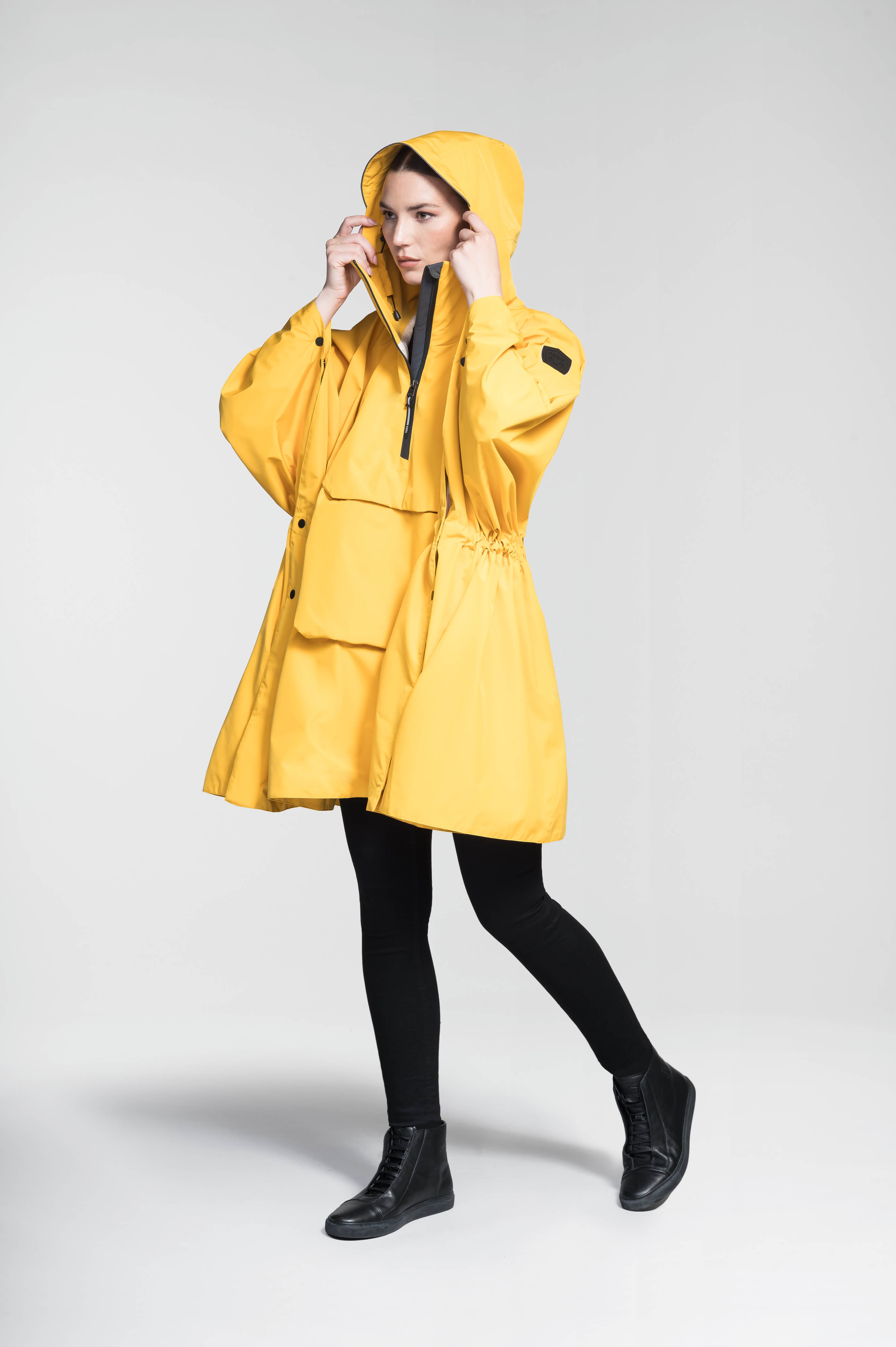 Hydra Unisex Performance Poncho in thigh length, non-removable hood, vertical half-zipper along centre front collar, hidden side-entry waist zipper pockets, adjustable webbing straps and snap closure cuffs, and packable to front kangaroo pocket with flap opening, in Old Gold