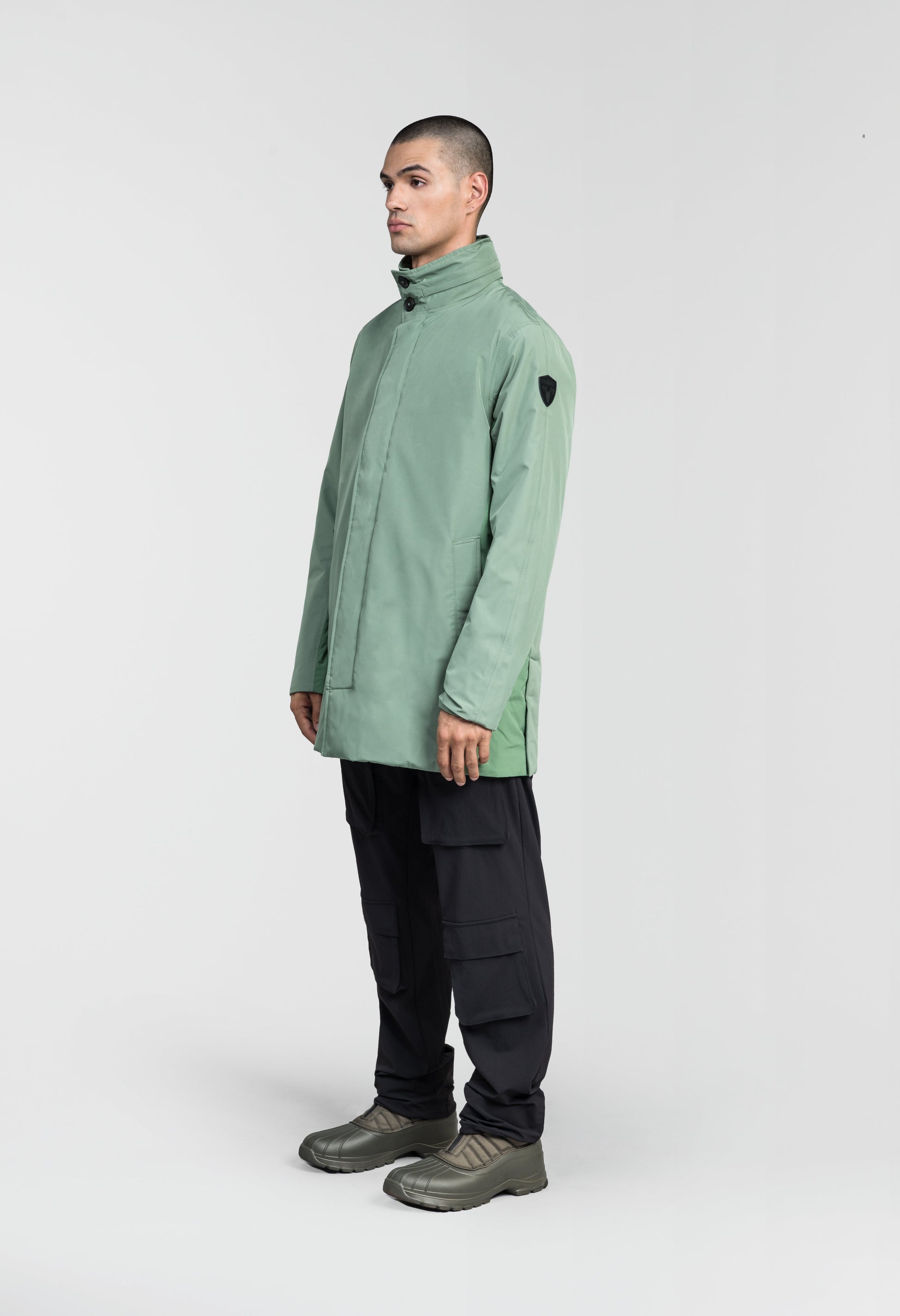 Pike Men's Tailored Mac Coat in thigh length, premium 3-ply Micro Denier fabrication at body and cire technical nylon taffeta fabrication at hood, premium 4-way stretch, water resistant Primaloft Gold Insulation Active+, hidden 2-way zipper with snap closure wind flap, single welt pockets with magnetic closure at waist, hidden snap placket at cuffs, pit zippers for ventilation, interior zipper pocket at right chest, and interior button pocket at left chest, in Comfrey