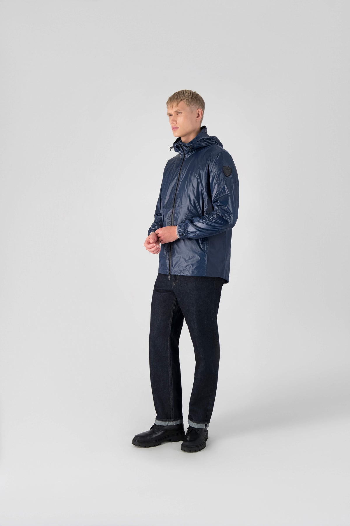 Stratus Men's Tailored Packable Rain Jacket in hip length, premium cire technical nylon taffeta and stretch ripstop fabrication, highly breathable mesh lining, hidden packable pocket, non-removable hood with adjustable draw cord, reflective piping along front and back, underarm grommets for extra breathability, back yoke with mesh ventilation, two waist zipper pockets, two interior zipper pockets, elastic cuffs with adjustable snap button, and adjustable interior draw cord at waist hem, in Marine