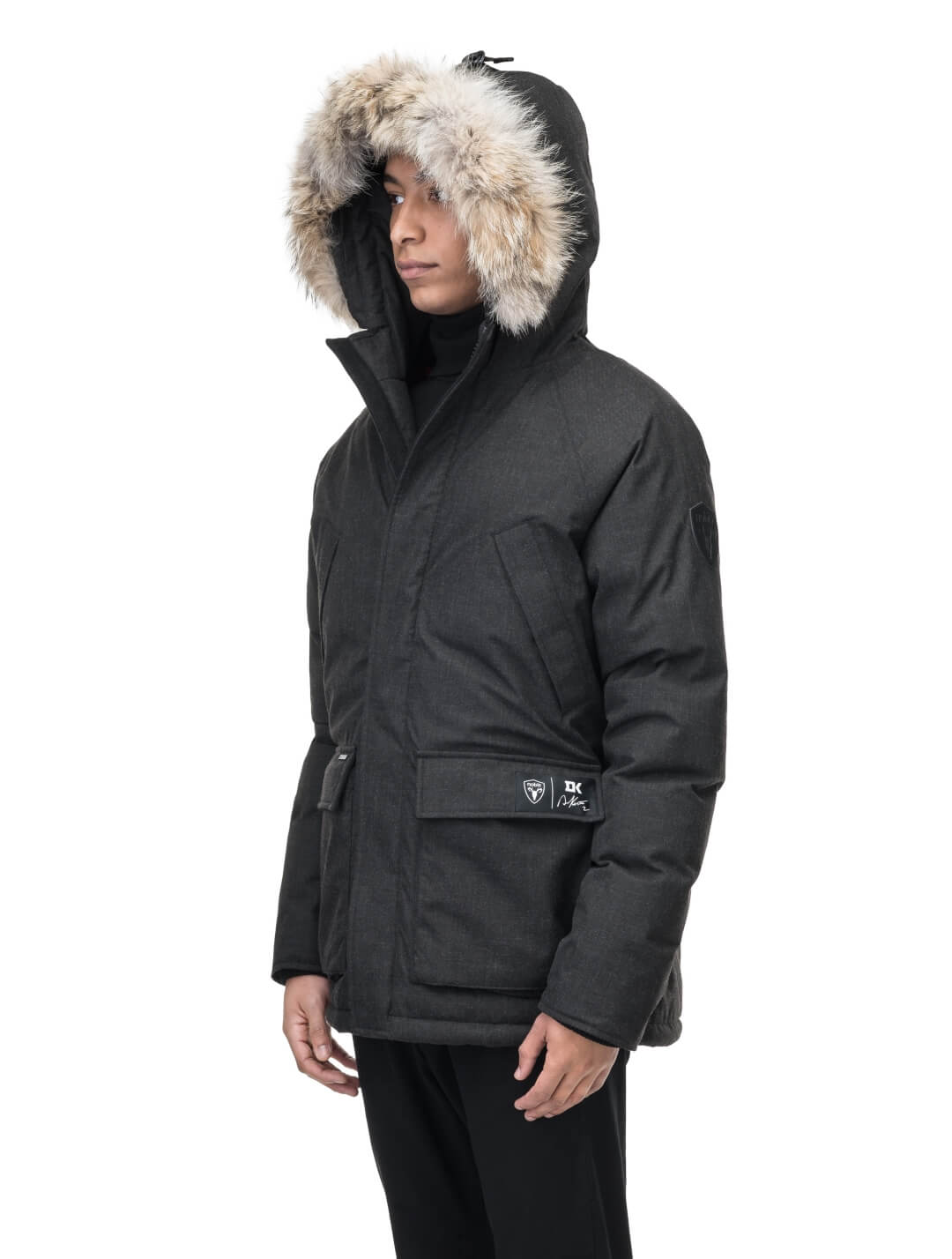 Duncan Keith Heritage Men's Parka in hip length, and features Canadian duck down insulation, non-removable hood with removable coyote fur trim, fleece-lined chest pockets, top and side entry waist pockets, adjustable waist cord, interior zipper pocket, and co-branding with Keith's signature on the left outer waist pocket, in H. Black